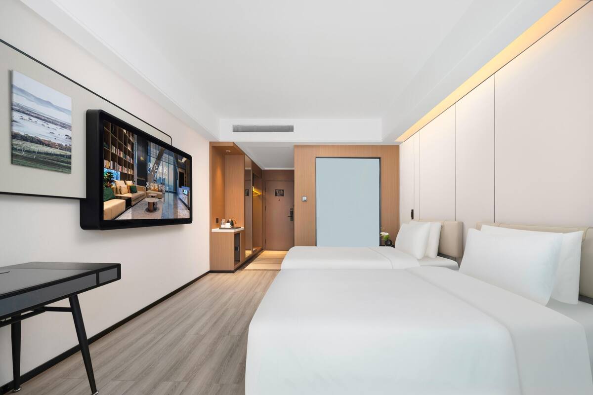 A modern hotel room with a large bed, a desk, and a television mounted on the wall.