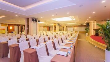 A conference room with rows of tables and chairs, a podium, and a large screen.