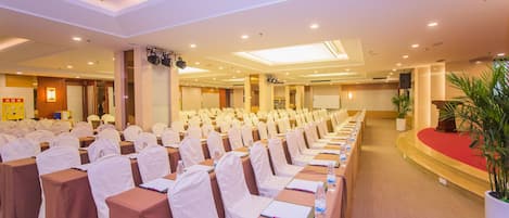 Un salón de conferencias con mesas y sillas en fila, un atril y una pantalla grande.