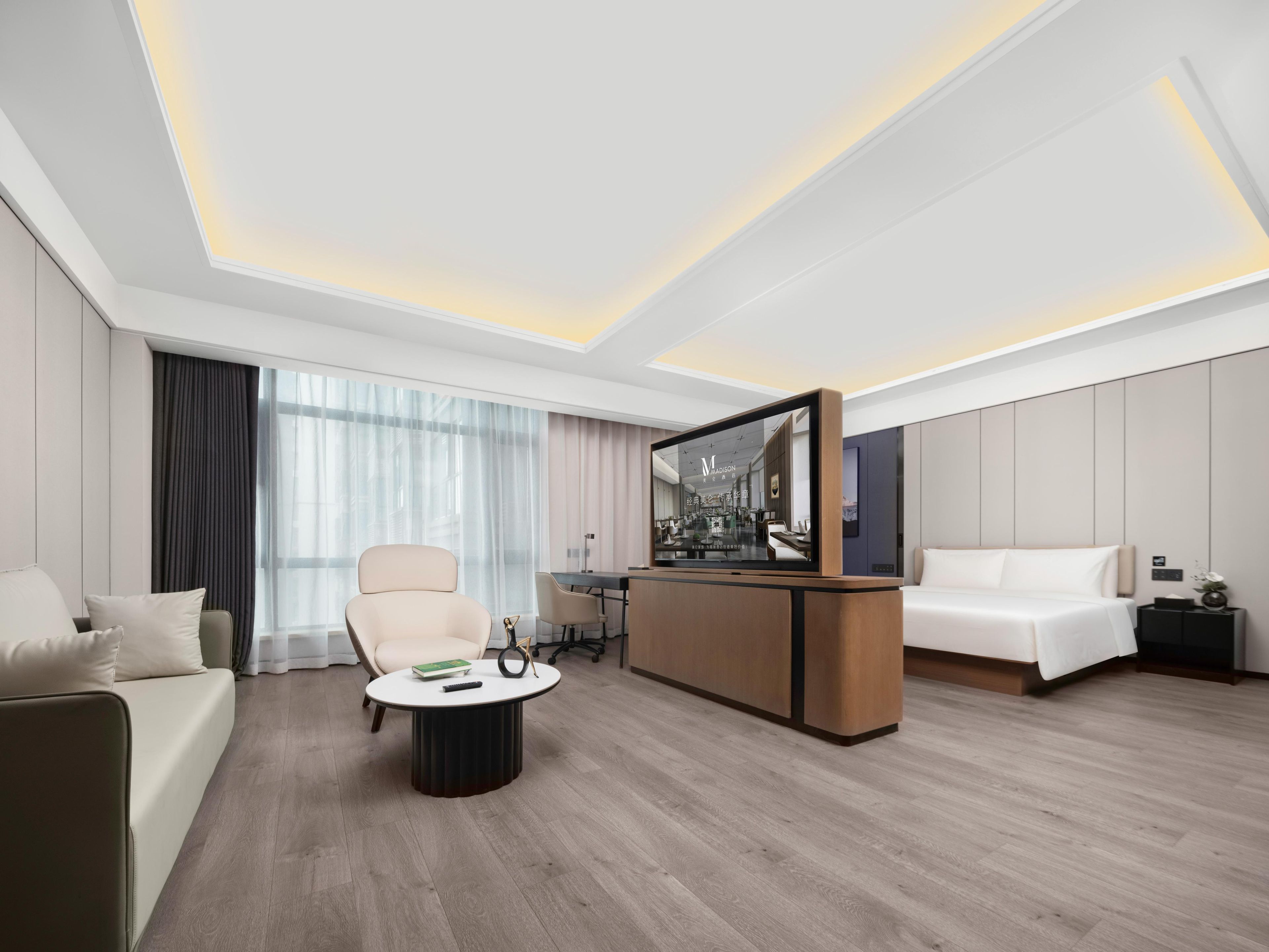 A modern hotel room with a sofa, a round coffee table, a TV, and a bed.