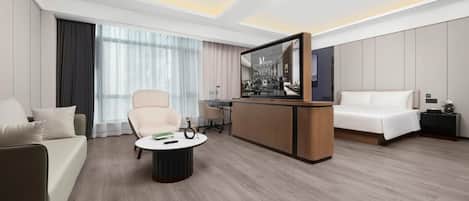 A modern hotel room with a sofa, a round coffee table, a TV, and a bed.