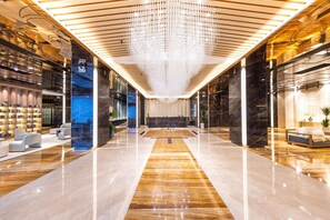 Un vestíbulo espacioso con un mostrador de recepción central, zonas de estar modernas y un candelabro decorativo.
