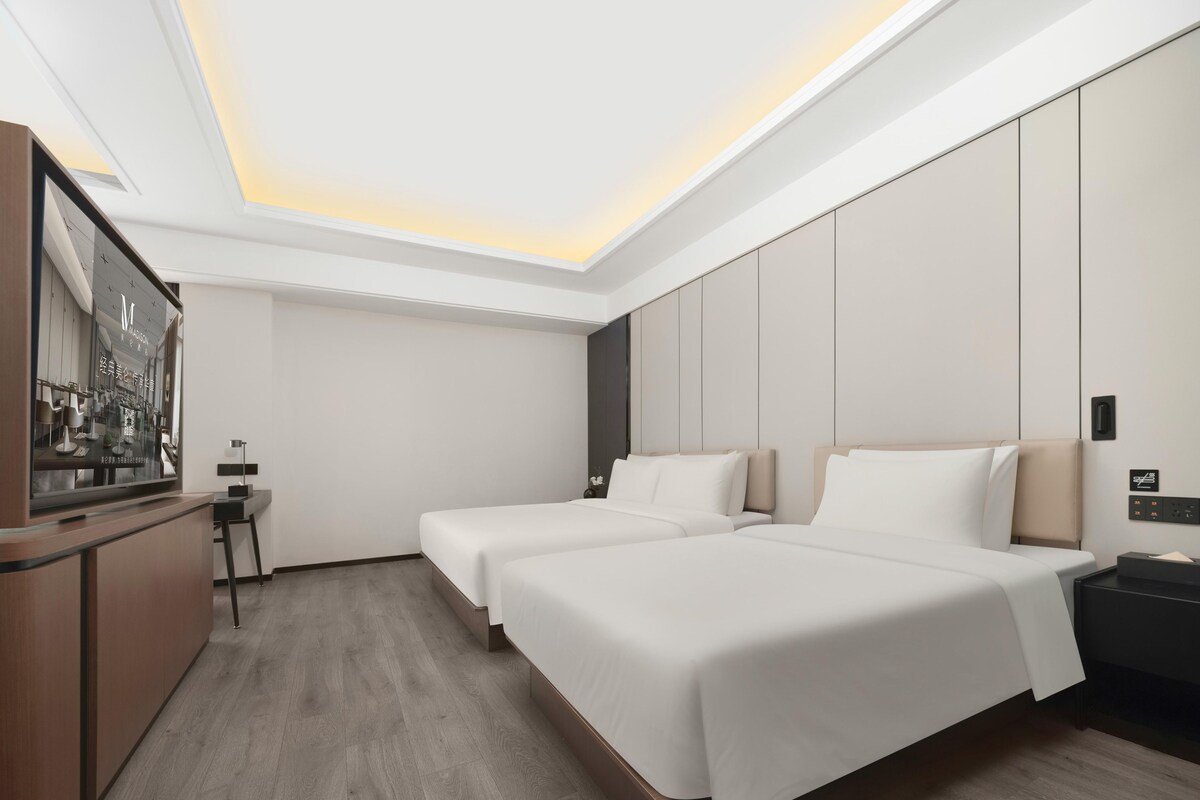 A modern hotel room with two beds, a desk, and a large window.