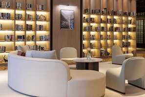 Una biblioteca moderna con sofás blancos, una mesa redonda para café y estanterías con repisas iluminadas.
