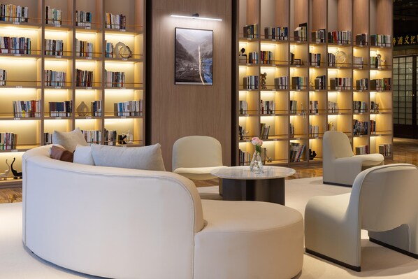 A modern library with white sofas, a round coffee table, and bookshelves with illuminated shelves. - Meilun Hotel Xian Qujiang Convention Center Mixc (Xi'an)