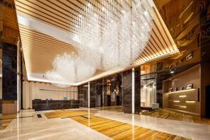 Un vestíbulo moderno con una recepción de madera, un gran candelabro y un piso de mármol.