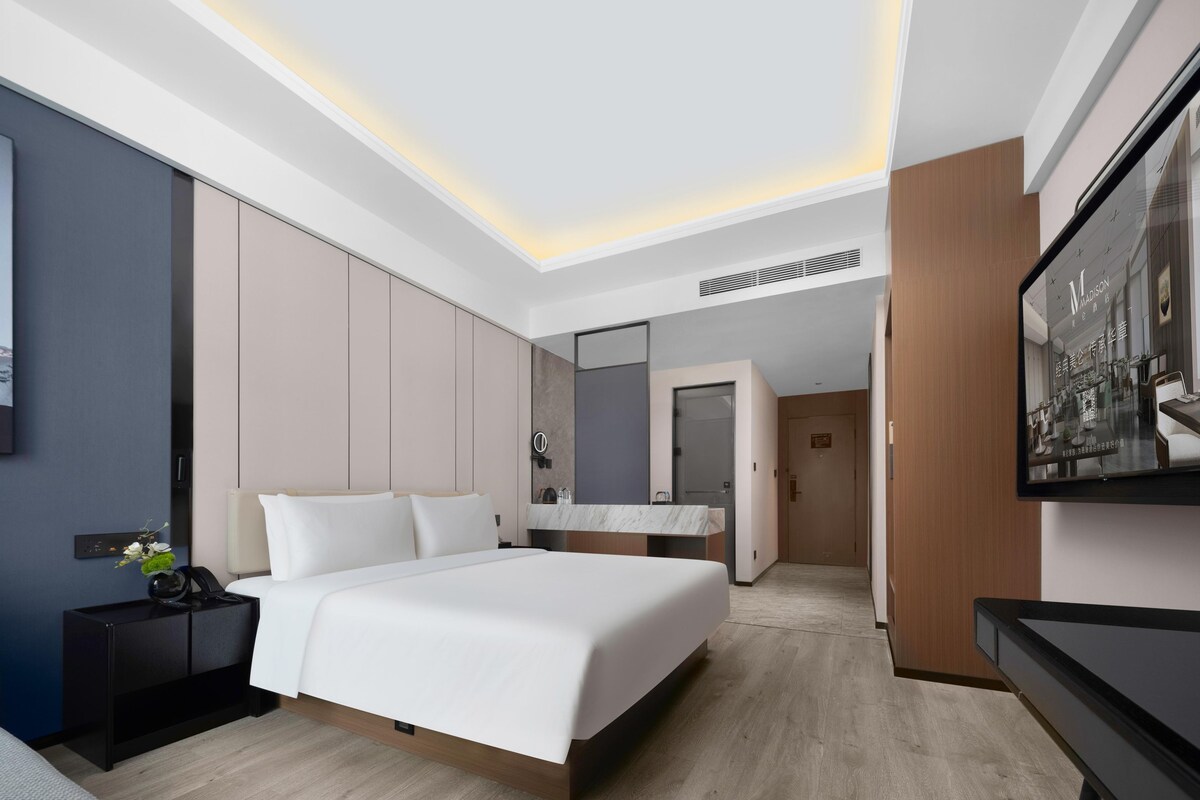 Habitació d'hotel moderna amb un llit gran, una taula de nit, un mirall i una televisió.