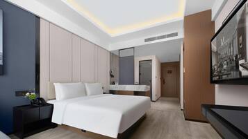 Quarto de hotel moderno com uma cama grande, mesa de cabeceira, espelho e televisão.