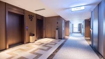 Corredor de hotel com portas de madeira, piso carpetado e placa indicando a direção do elevador.