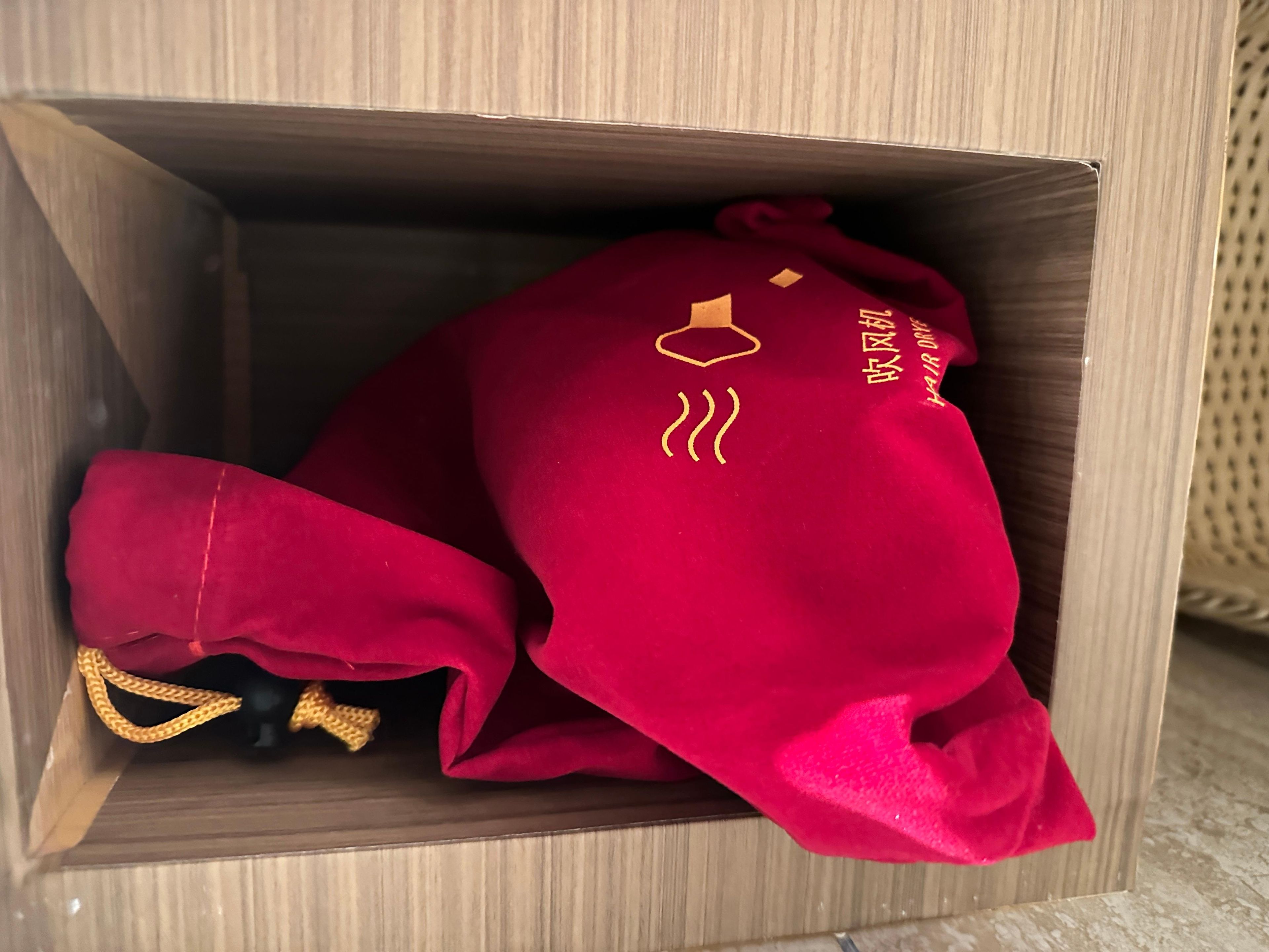 Uma caixa de madeira contendo uma bolsa vermelha com bordado dourado e uma corrente de ouro.