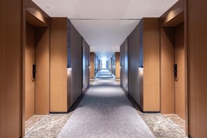 A long, narrow hallway with wooden walls and a carpeted floor, leading to a bright exit at the end. - Meilun Hotel Xian Qujiang Convention Center Mixc (Xi'an)