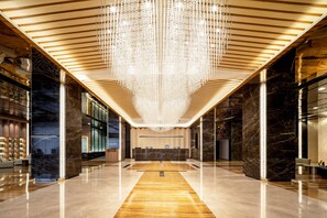 Un vestíbulo amplio con una recepción central, un candelabro y suelos de mármol.