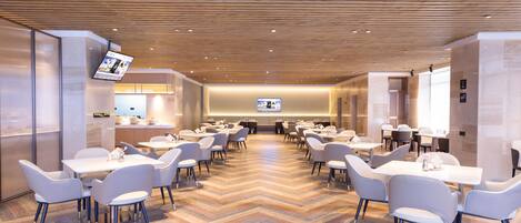 A spacious dining area with multiple tables and chairs, a wooden ceiling, and a modern interior design.