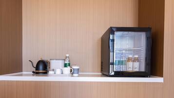 A kitchenette with a kettle, cups, a water bottle, and a refrigerator.