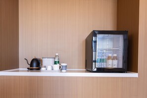 A kitchenette with a kettle, cups, a water bottle, and a refrigerator. - Meilun Hotel Xian Qujiang Convention Center Mixc (Xi'an)