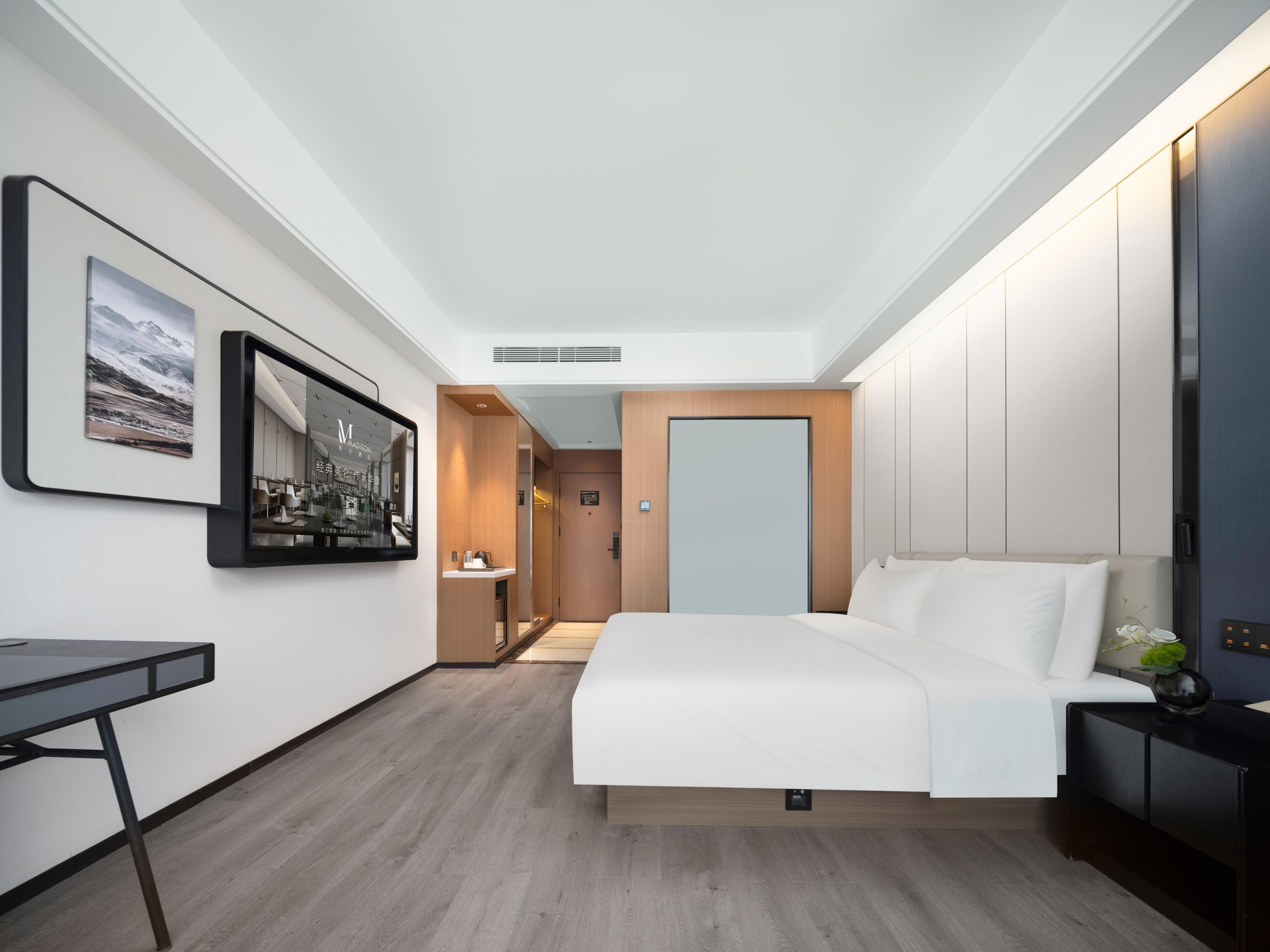 Une chambre d’hôtel moderne avec un grand lit, un bureau, un miroir et un tableau encadré au mur.