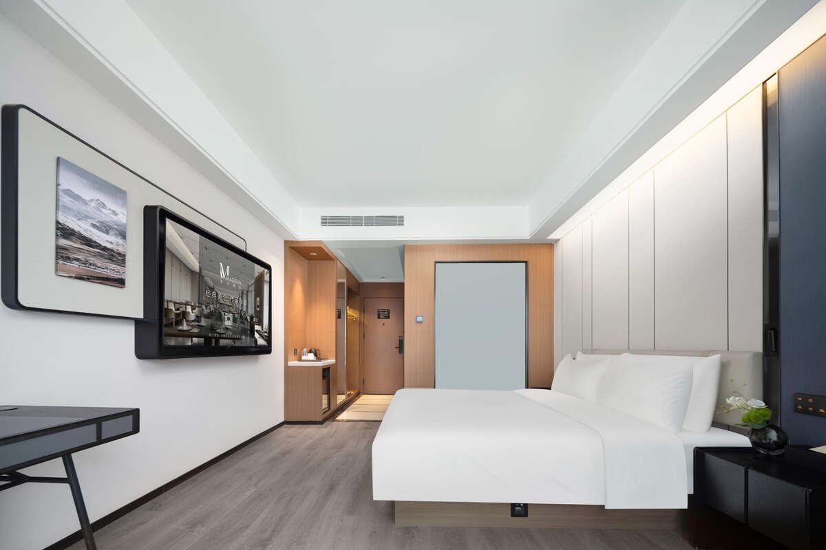 Une chambre d’hôtel moderne avec un grand lit, un bureau, un miroir et un tableau encadré au mur.