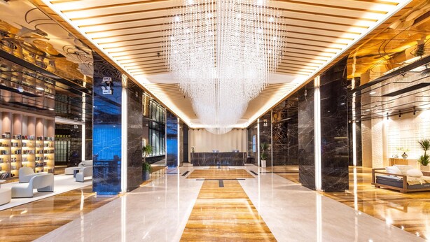 Een ruime lobby met een centraal gelegen receptiebalie, moderne zithoeken en een decoratieve kroonluchter.