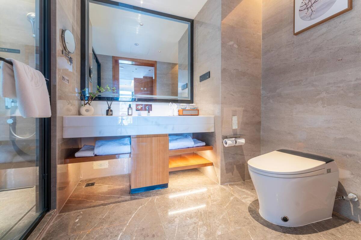 Ein modernes Badezimmer mit einem großen Spiegel, einer weißen Toilette und einem Waschtisch mit Spüle und Handtuchhalter.