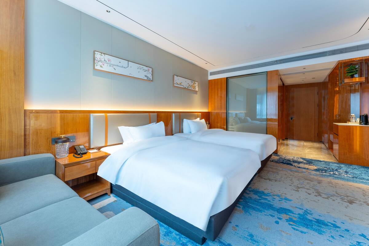Ein modernes Hotelzimmer mit einem großen Bett, Nachttischen, einer Sitzecke und einem durch eine Glastür sichtbaren Badezimmer.