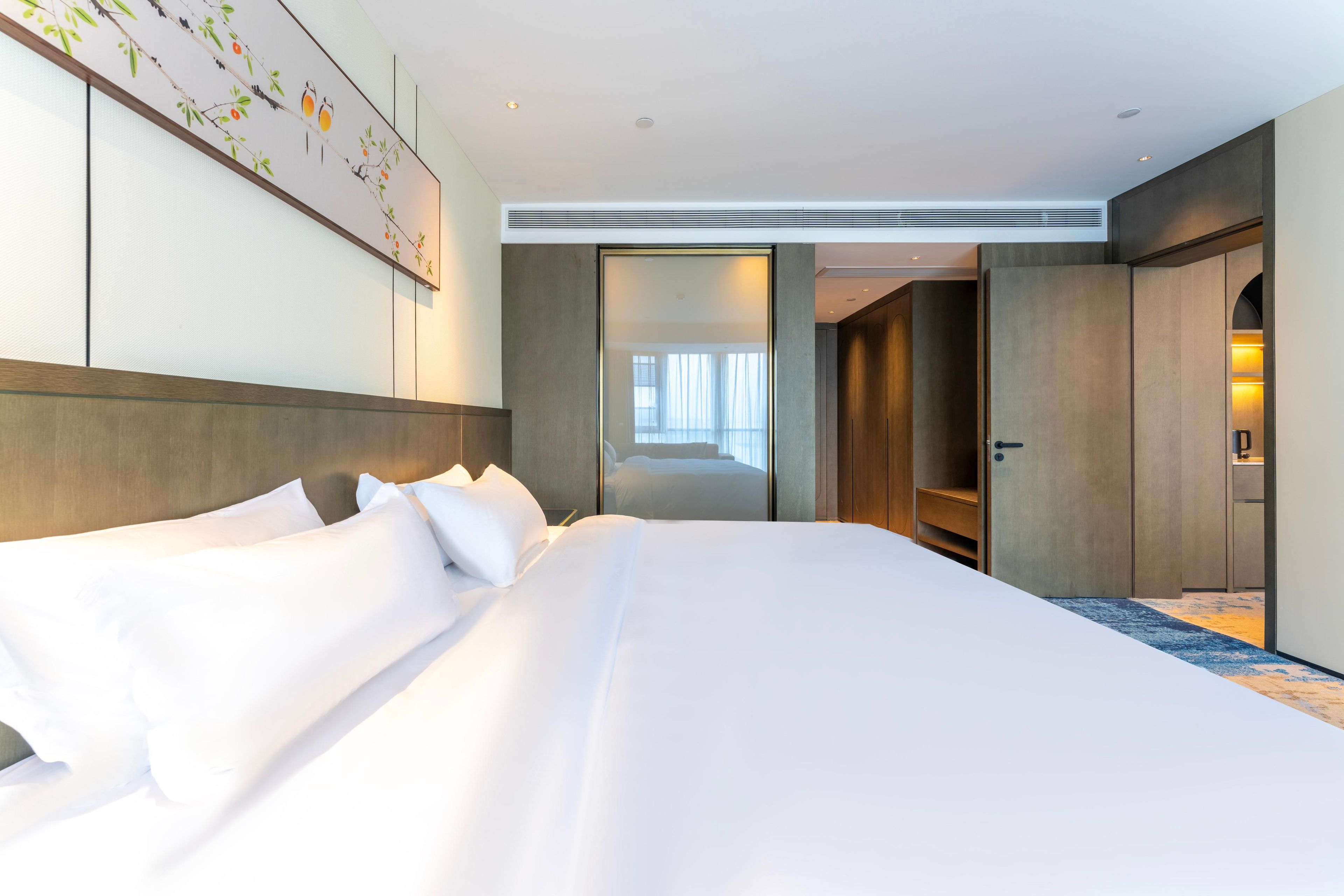A hotel room with a large bed, a wardrobe, a mirror, and a painting on the wall.