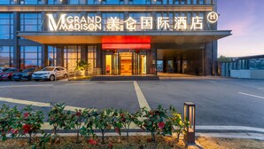 A hotel entrance with a modern facade, illuminated signage, and a parking area with several cars. - Grand Madison Hotel Quzhou High-speed Railway Sta (Quzhou)