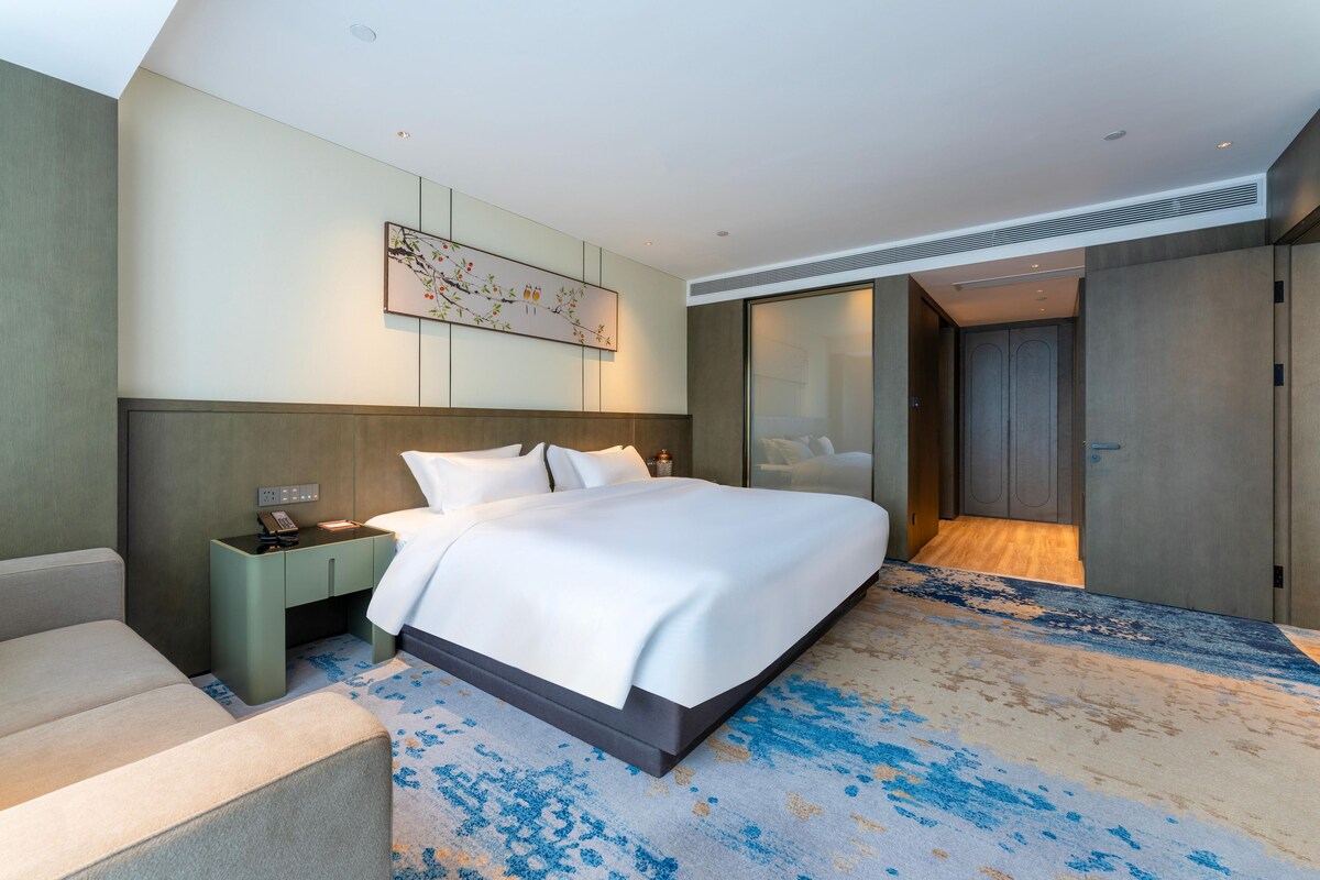 Een moderne hotelkamer met een groot bed, een nachtkastje met een telefoon, een kunstwerk aan de muur en een vloerbedekking.