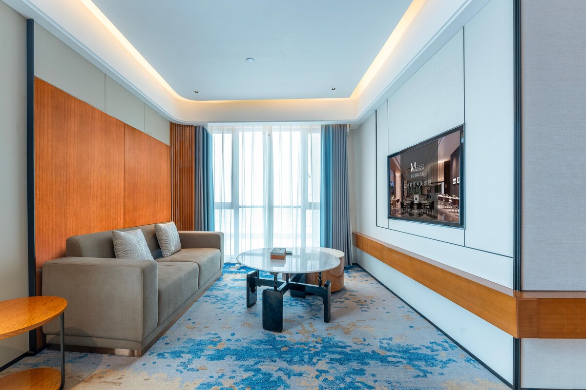 Ein modernes Hotelzimmer mit einer Sitzecke, einem runden Tisch und einem großen Fenster.