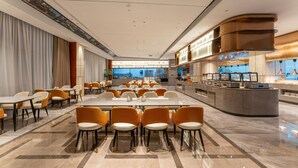 A modern hotel lobby with a long reception desk, multiple seating areas, and a view of the cityscape through large windows.