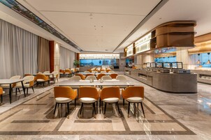 Un moderno vestíbulo de hotel con un mostrador de recepción alargado, varias zonas de estar y vistas a la ciudad a través de amplias ventanas.