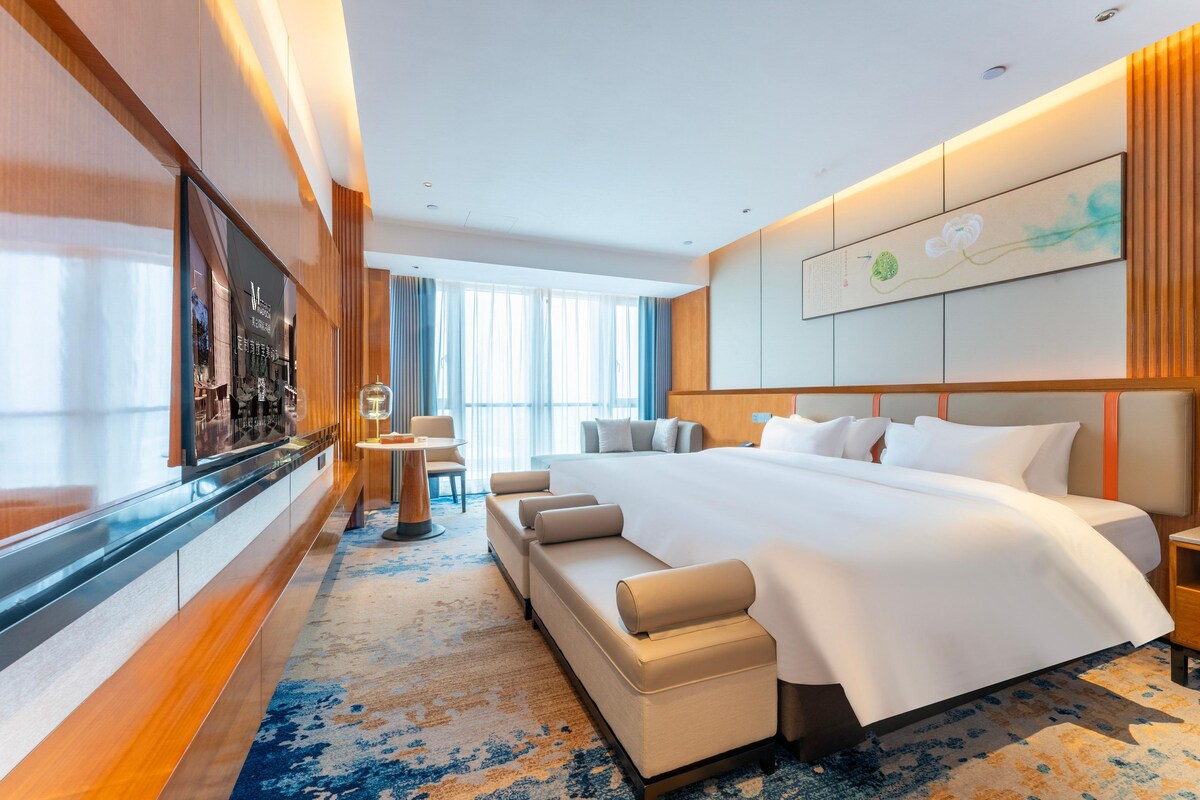 Een moderne hotelkamer met een groot bed, een bank, een televisie en uitzicht op de stad.