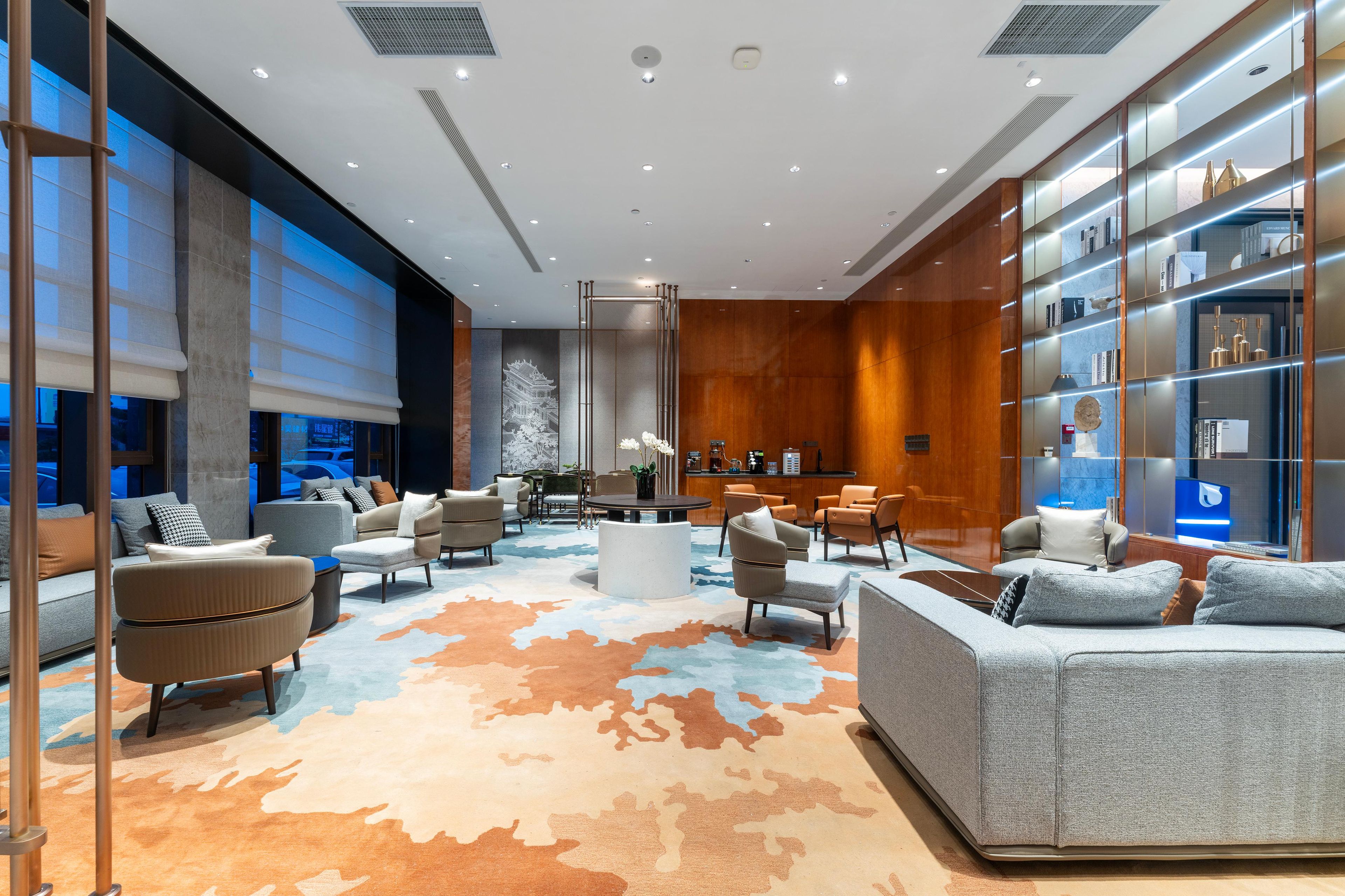 A modern lobby with a central seating area, a reception desk, and a large bookshelf.