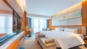 A modern hotel room with a large bed, a sofa, a TV, and a view of the city.