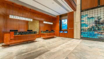 Un área de recepción con paneles de madera, mostradores de mármol y una gran pantalla digital.