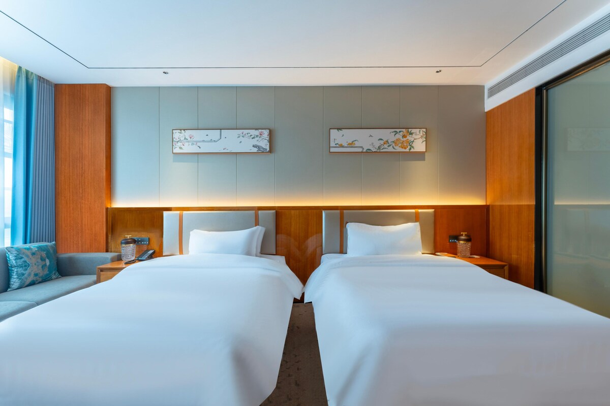 Een hotelkamer met twee bedden, een bank en een groot raam.