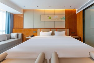 Una habitación de hotel moderna con una cama grande, un sofá, una mesita de noche y una obra de arte colgada en la pared.