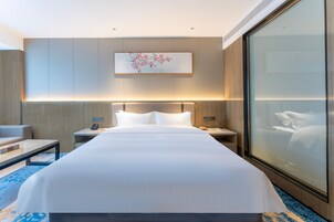 Una habitación de hotel moderna con una cama grande, mesitas de noche, un escritorio y un ventanal con vistas.