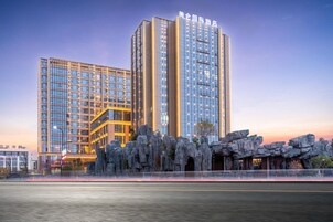 Un hotel moderno con varios edificios de gran altura, que destaca por su entrada con una formación rocosa y una fachada bien iluminada.