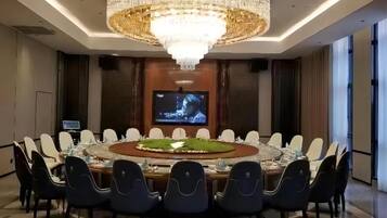 Un salón de conferencias con una gran mesa redonda, varias sillas, un candelabro, una pantalla de televisión y una pantalla pequeña sobre la mesa.