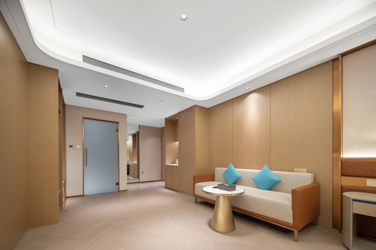 Un moderno vestíbulo de hotel con piso de madera, un sofá con cojines azules, una mesa dorada y un mostrador de recepción de madera.
