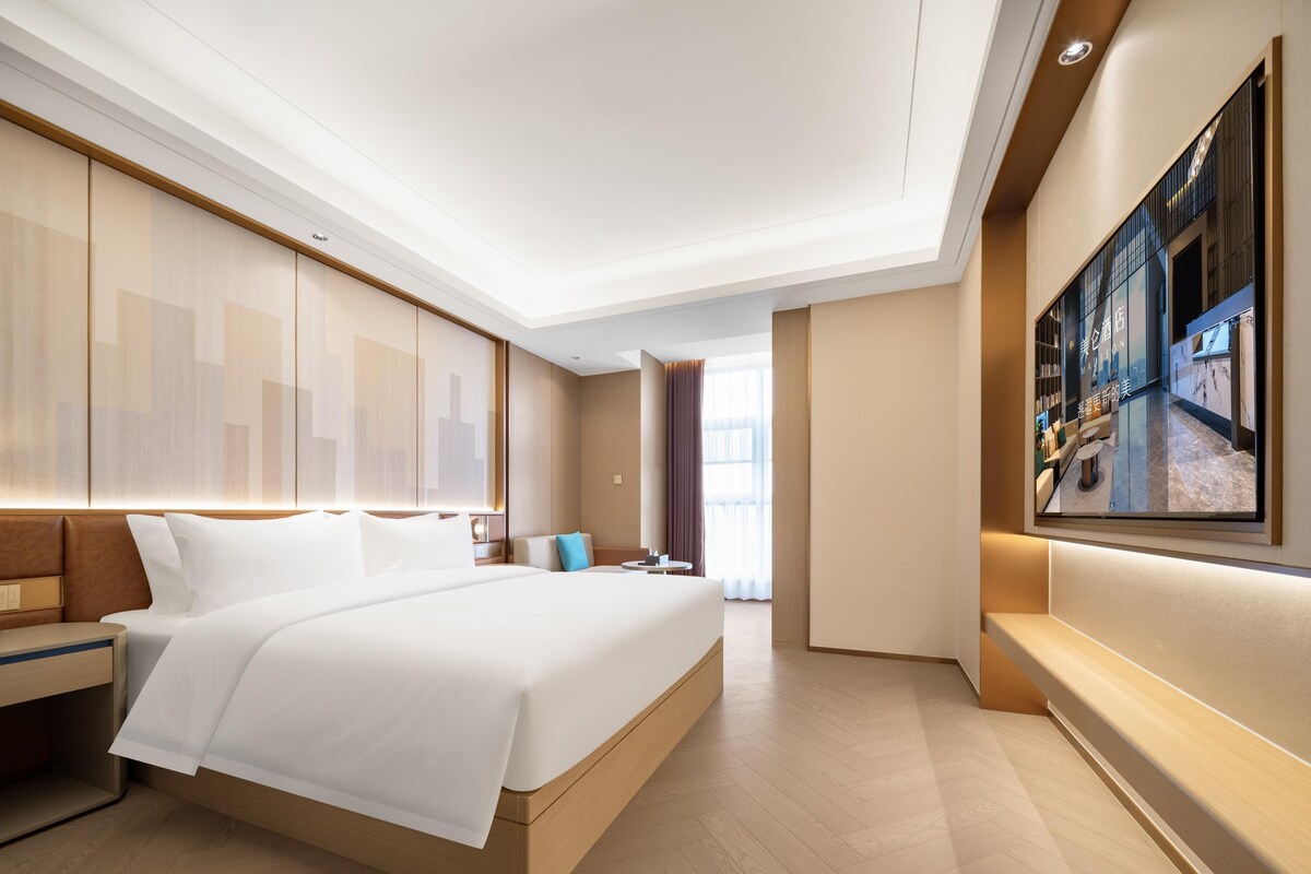 Una habitación de hotel moderna con una cama grande, una zona de estar y un televisor montado en la pared.