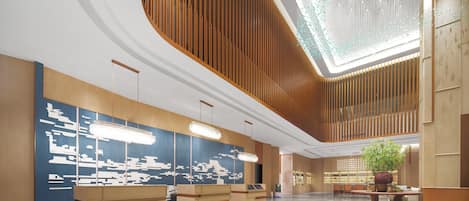 A spacious lobby with a modern design, featuring a reception desk, seating area, and a large plant.