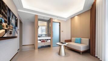 Un moderno vestíbulo de hotel con un sofá, una mesa de centro y un baño visible a través de un panel de vidrio.