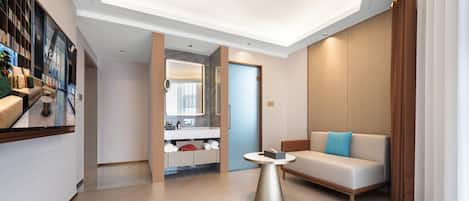 Un moderno vestíbulo de hotel con un sofá, una mesa de centro y un baño visible a través de un panel de vidrio.