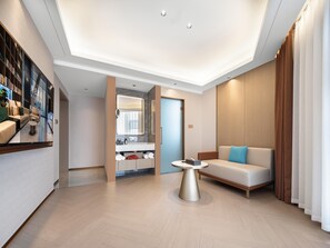 Un moderno vestíbulo de hotel con un sofá, una mesa de centro y un baño visible a través de un panel de vidrio.