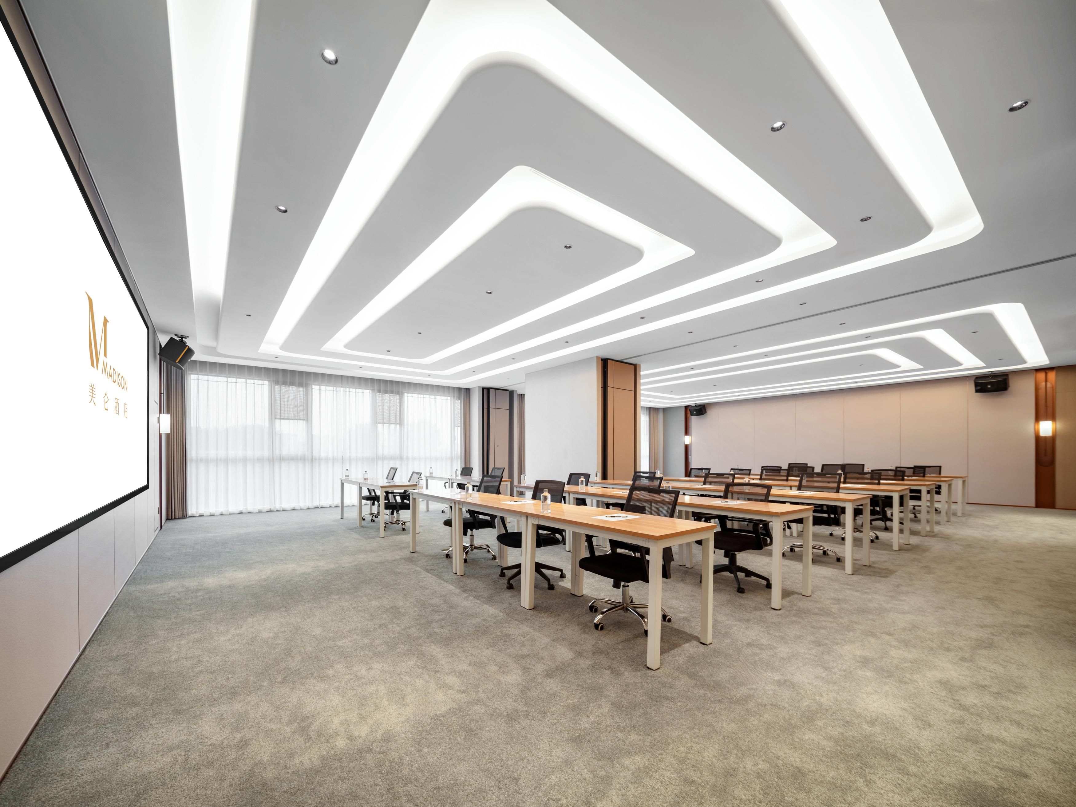 Una sala de conferencias moderna con una mesa larga, sillas y una pantalla de proyector.