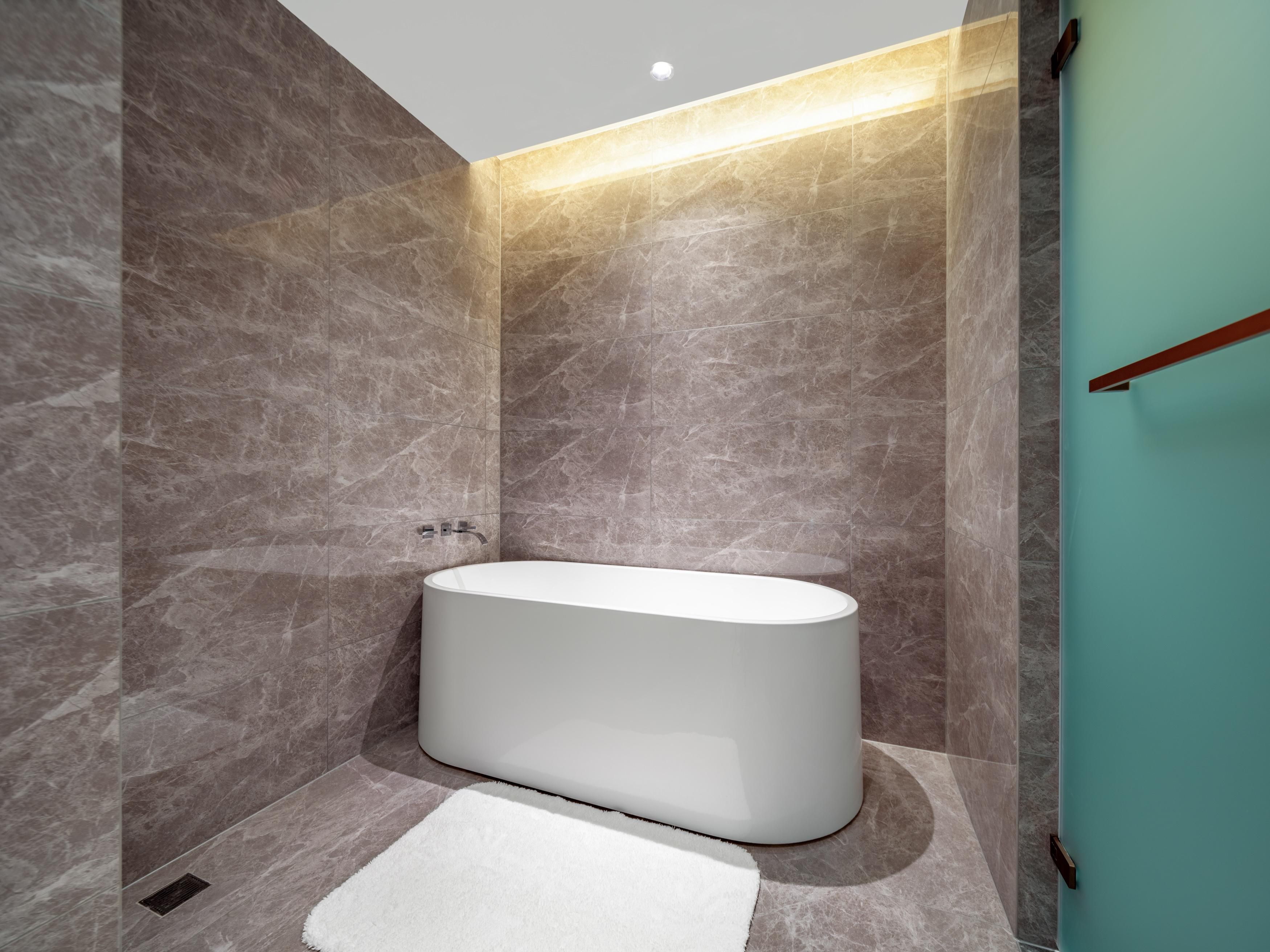 A modern bathroom with a freestanding bathtub, marble walls, and a teal accent wall.
