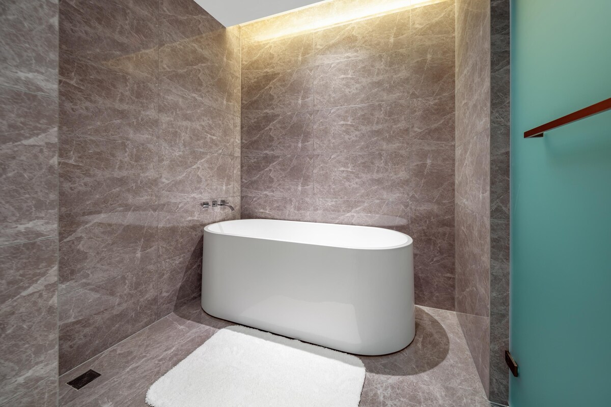 Une salle de bain moderne avec une baignoire sur pieds, des murs en marbre et un mur d’accent de couleur turquoise.