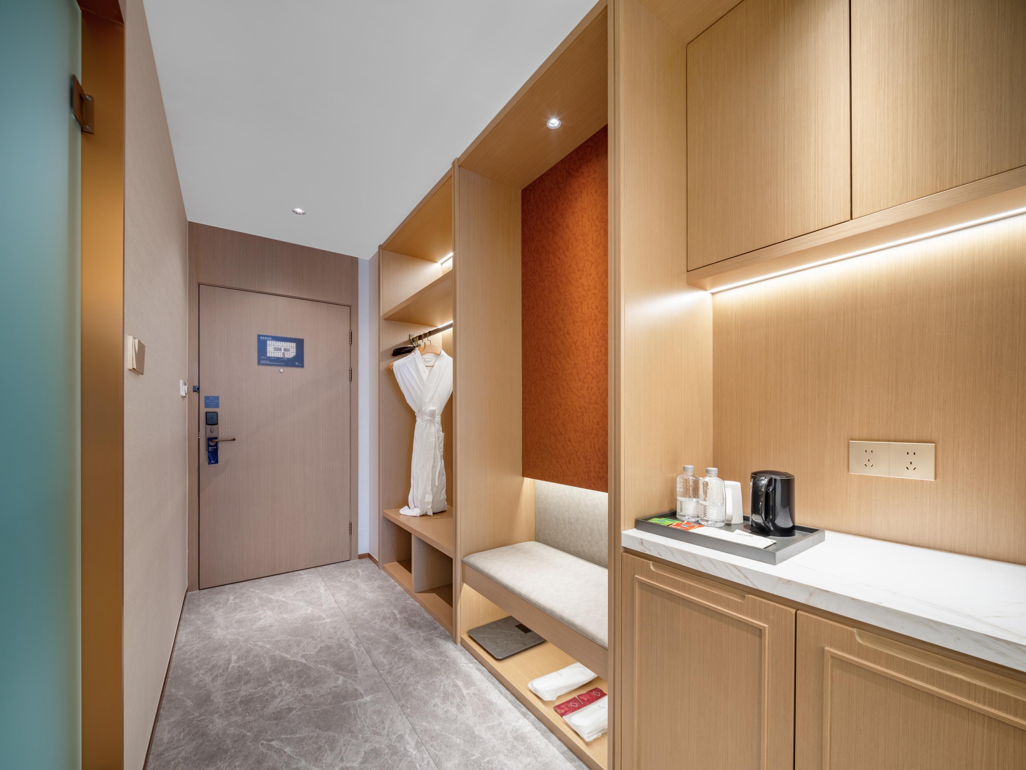Habitación de hotel con armario de madera, una bata colgada, una pequeña zona de estar y un tocador con artículos de aseo.