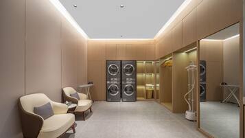 A modern laundry room with two chairs, a small table, and a large mirror.